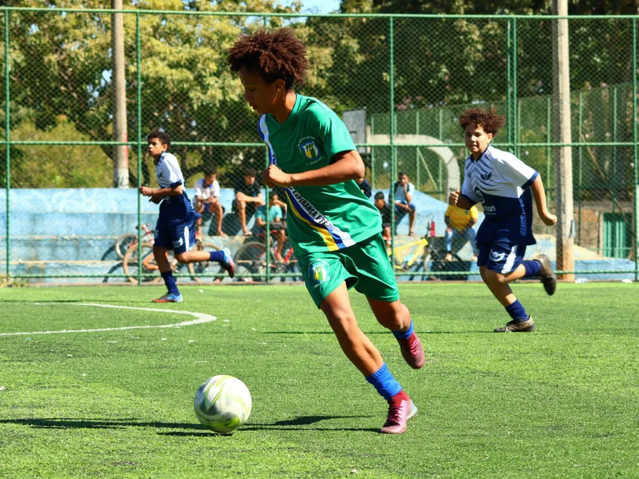 Menino de uniforme verde conduzindo a bola em velocidade — aluno da Transbatista em jogo