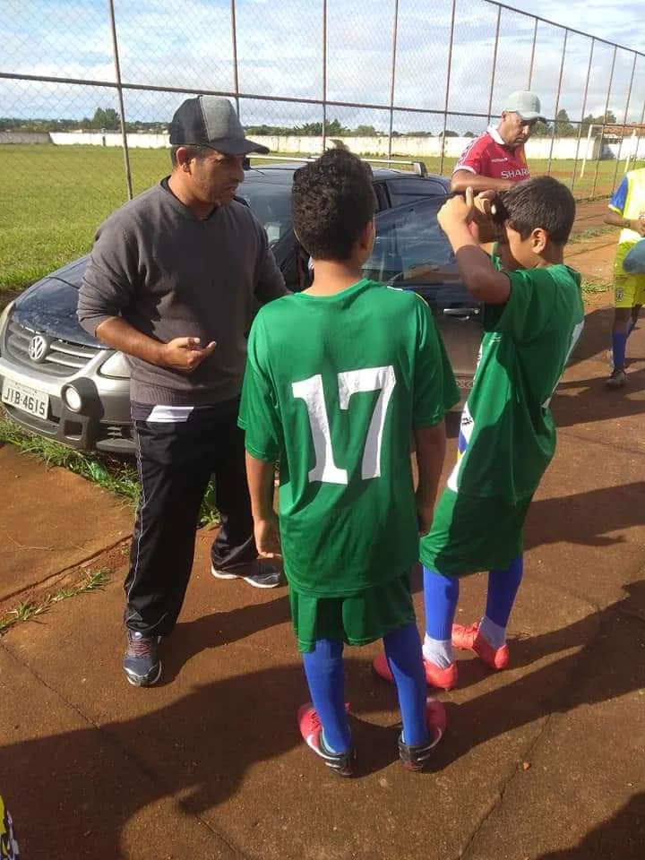 Treinador conversando com dois alunos de uniforme verde