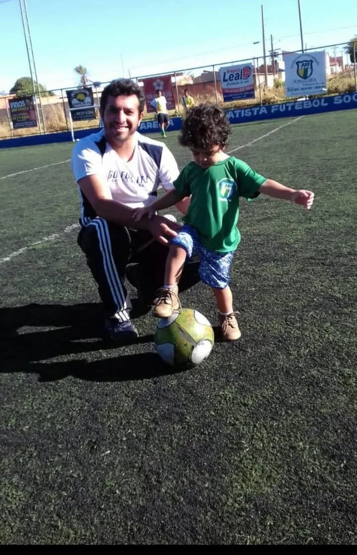Treinador agachado ao lado de uma criança pequena com a bola